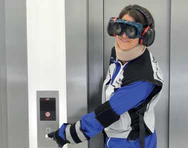 Person im Alters-Simulationsanzug vor Fahrstuhl